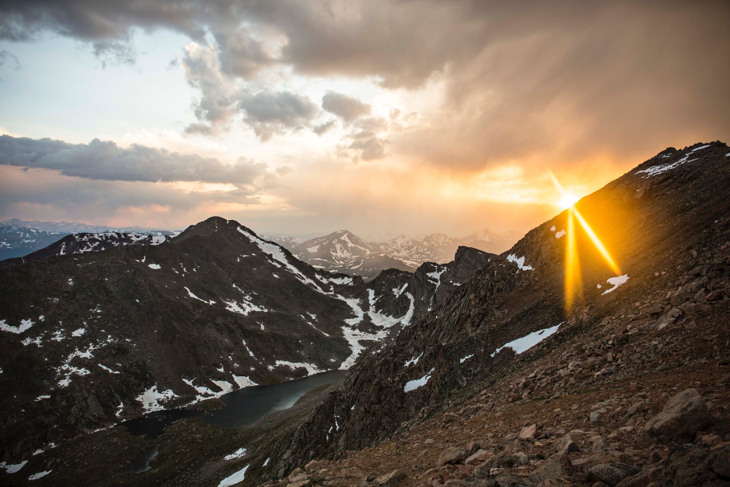 evershot-b_Db88WWLSY-unsplash The peaks of mountains and a lake nestled among them with the sun glaring from just above the ridgeline