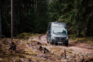 a black mercedes sprinter van on a dirt road in the woods