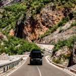 A black sprinter van driving on a highway through mountains